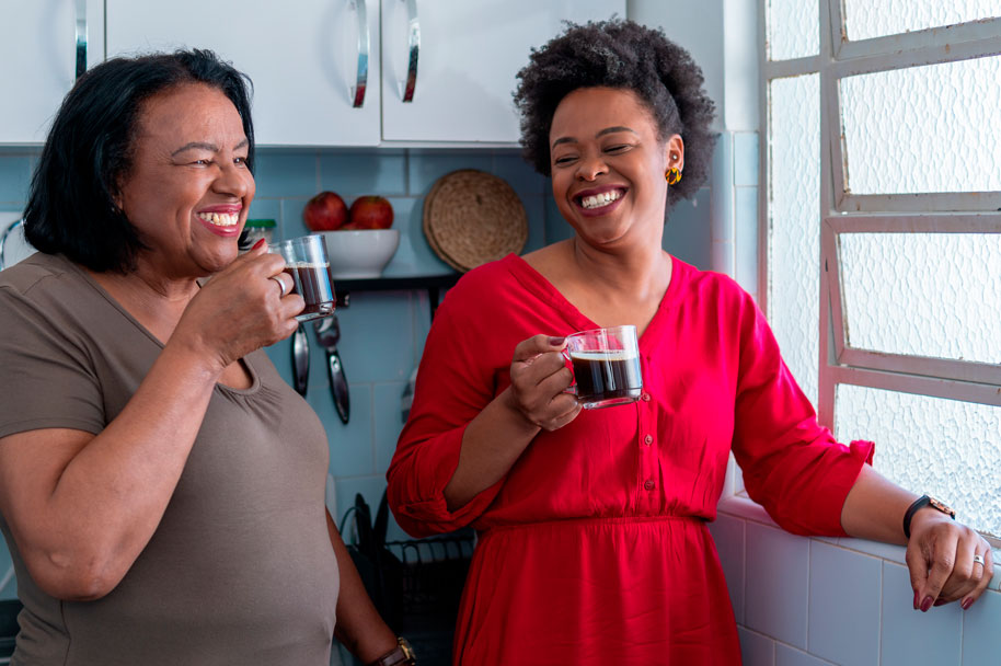 Duas mulheres negras tomam café. Uma usa blusa vermelha e a outra marrom. Ambas falam sobre a saúde da população negra no Brasil