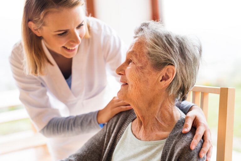 Paciente de idade, sentada olhando para uma enfermeira. Atenção Primária à Saúde